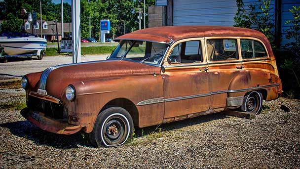 Old rusted station wagon in front yard.