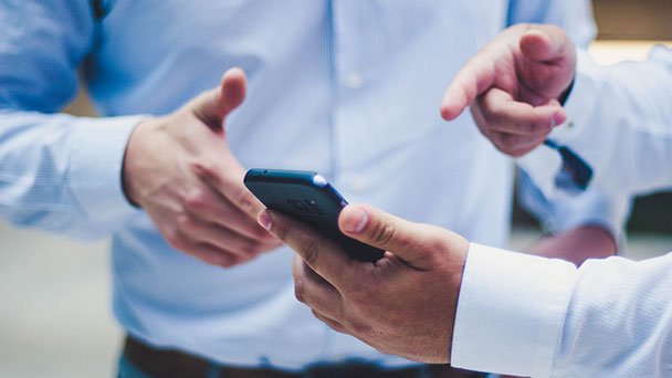 Two men looking at a mobile phone doing research on car sales.