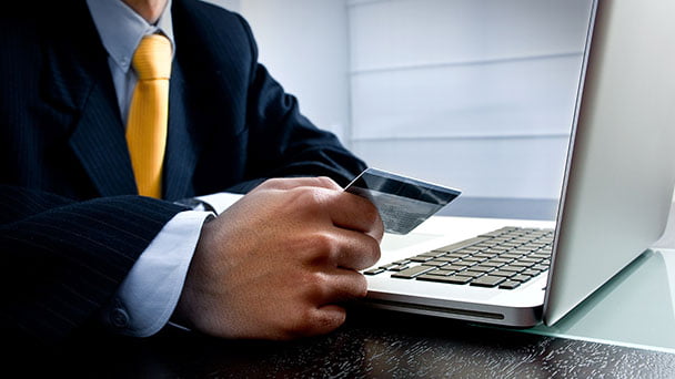 Man in business suit holding bank card in front of computer.