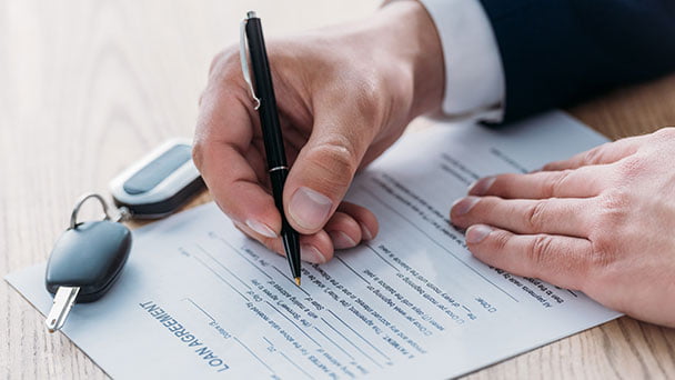 Man signing a car loan agreement with keys on table.