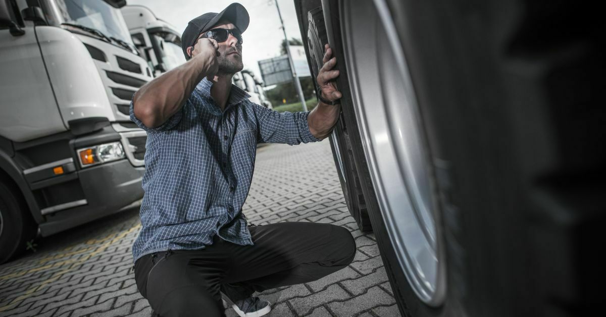 Driver kneeling down next to large truck tyre as he inspects it when considering to buy.