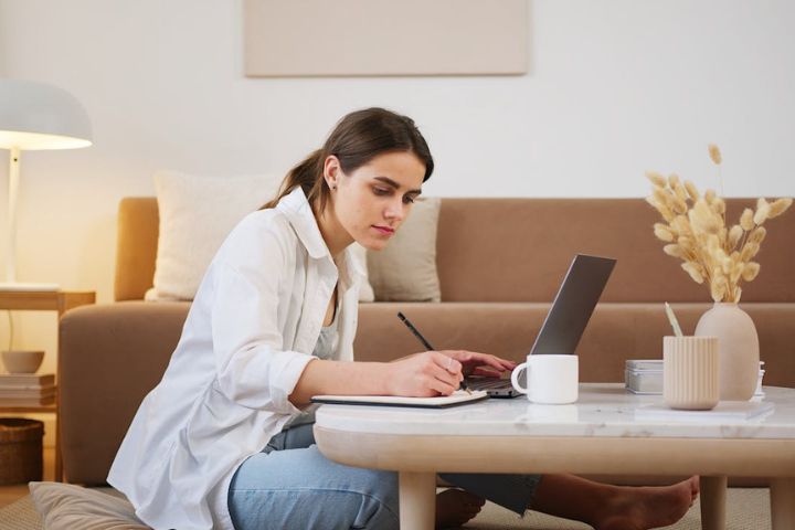 Young woman using laptop and taking notes.